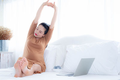 Young woman using mobile phone while sitting on bed