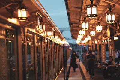 People walking on illuminated street amidst train