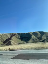 Scenic view of road by mountains against clear blue sky