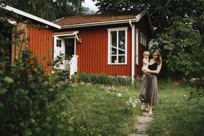 Woman standing by house against trees and plants