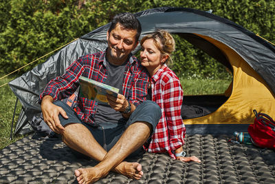 Couple planning next trip while sitting with map by tent. concept of camp life