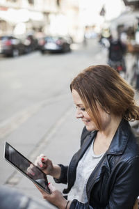 Smiling mid adult woman using digital tablet on sidewalk bench