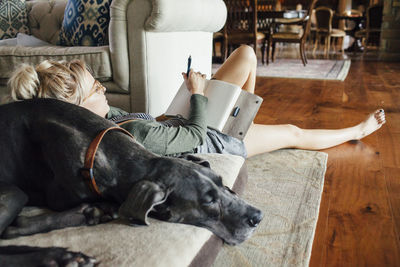 Woman writing diary while reclining on great dane