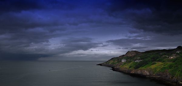 Scenic view of sea by landscape against cloudy sky