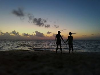 Silhouette men on beach against sky during sunset