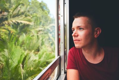 Young man looking through window while traveling in train