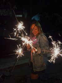 Smiling young woman holding sparklers at night