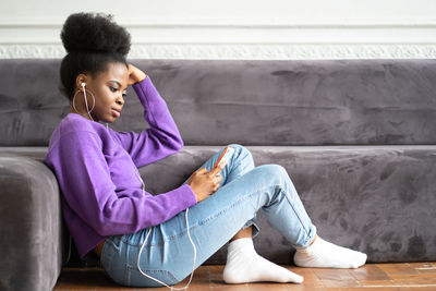 Side view of young woman using smart phone siting on floor