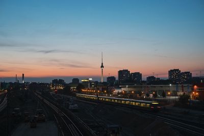 Mid distant view of illuminated fernsehturm against sky during sunset