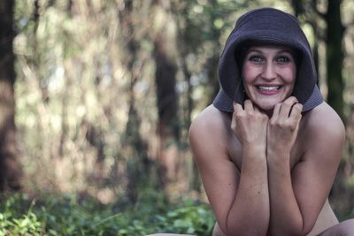 Portrait of shirtless woman sitting against tree