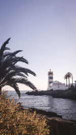 Lighthouse by sea against clear sky