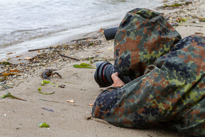 Person in hooded shirt photographing at sea shore