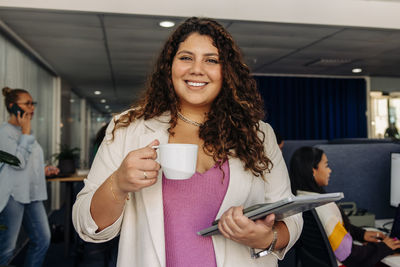 Portrait of smiling female entrepreneur holding coffee cup at office