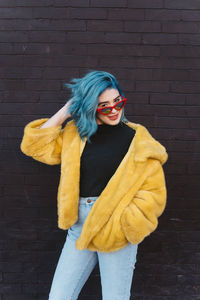 Portrait of woman wearing coat and sunglasses while standing against brick wall