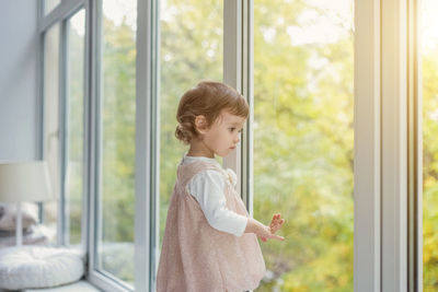 Rear view of girl standing by window at home