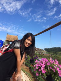 Portrait of smiling woman standing by railing against sky