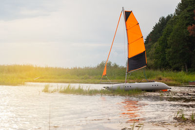 Inflatable sailing catamaran with raised sails on the river near the shore. summer sports concept