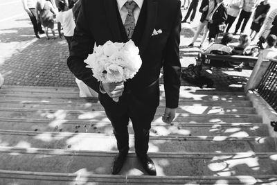 Low section of groom standing with bouquet on steps