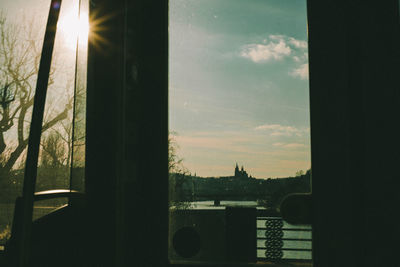 Silhouette trees by building against sky during sunset seen through window