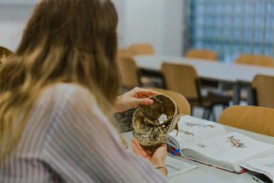 Rear view of woman holding skull at classroom