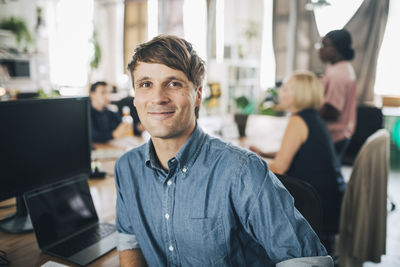 Portrait of confident businessman sitting at desk in creative office