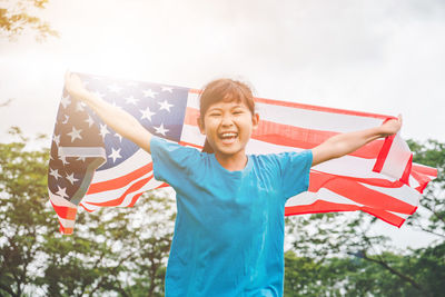 Happy teenage girl with american flag against trees