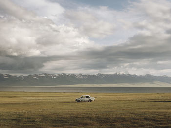 Car on field against cloudy sky