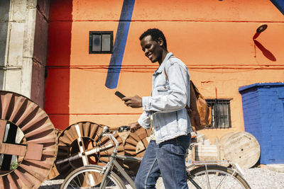 Relaxed young amn commuting in the city with hos bicycle, using smartphone