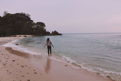 Rear view of woman standing at beach against clear sky during sunset