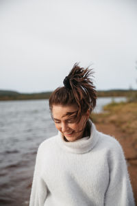 Portrait of young woman standing at beach against sky