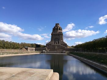 View of temple by lake against sky