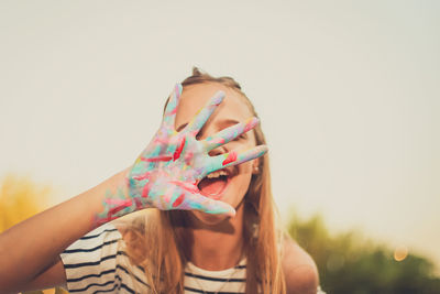 Close-up of girl with messy painted hands against clear sky