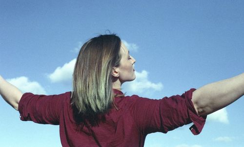 Portrait of woman with arms raised against sky