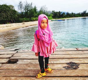 Cute girl in headscarf standing on pier over lake