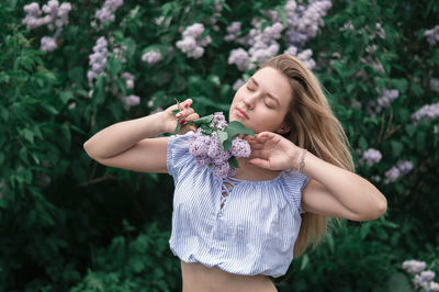 Young woman holding flower while standing against plants