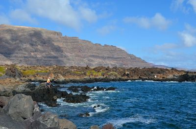 Man fishing while standing on rock by sea against mountain