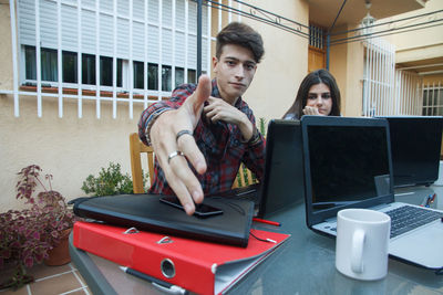 Portrait of confident businessman sitting with colleague while using laptop at table