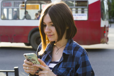 Woman using phone on road against bus