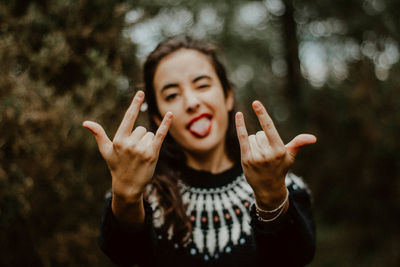 Portrait of woman gesturing horn sign against trees