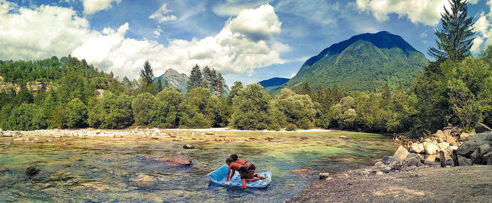 Panoramic view of mother and son duo on air mattress against trees and mountains against sky