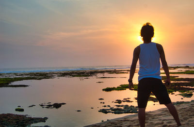 Rear view of man standing on beach during sunset