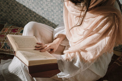 Midsection of woman reading koran at home