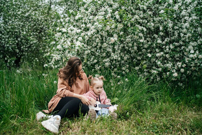 Young mother and baby daughter play the ukulele in a blooming apple orchard in nature