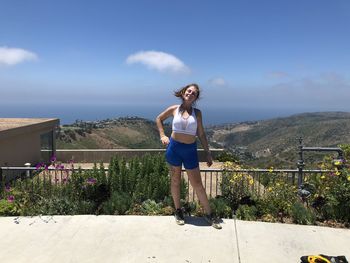 Young woman standing by plants against sky