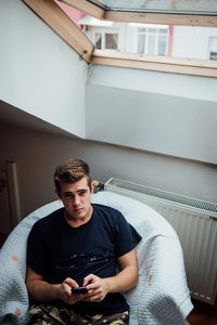 Portrait of young man using mobile phone while sitting on chair