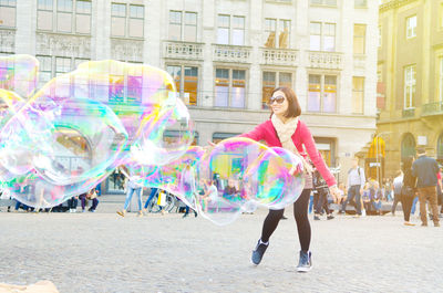 Woman playing with large bubbles on street in city