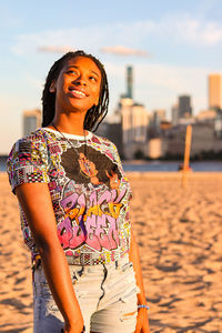 Young woman standing on beach with city background