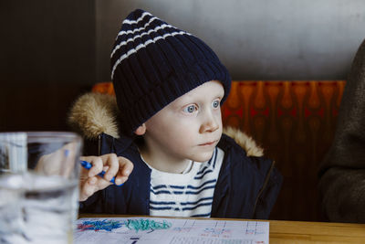 Boy colouring in red restaurant booth wearing white and navy waiting