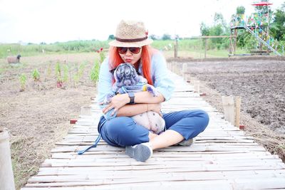 Woman with dog sitting on footbridge at agricultural field