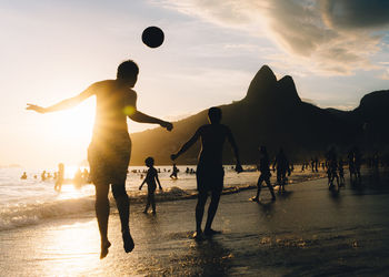 People playing with ball at beach against sky during sunset